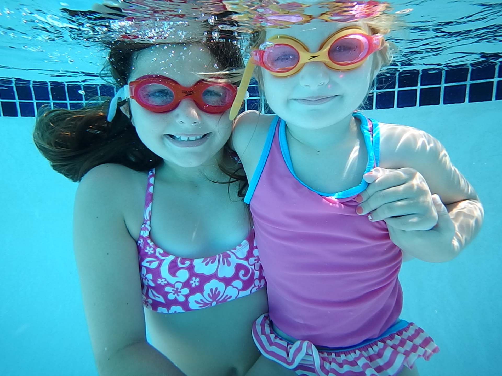 Two joyful young girls, aged 6 and 3, gleefully swimming underwater